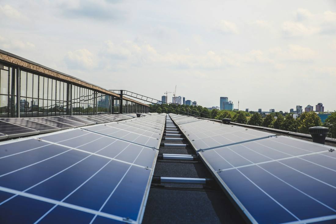 Rows of solar panels across a commercial rooftop with a city skyline behind
